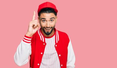 Beyzbol üniforması giyen sakallı genç adam başarılı bir fikirle işaret ediyor. Heyecanlı ve mutlu. Bir numara.. 