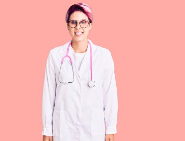 Pembe saçlı, doktor üniforması giyen, yüzünde mutlu ve havalı bir gülümseme olan genç ve güzel bir kadın. şanslı kişi. 