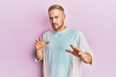 Kafkasyalı genç bir adam günlük giysiler giyiyor, tiksinti ifadesi takınıyor, tiksinti ifadesi takınıyor ve tiksinti ifadesi takınıyor. Eller havada. 