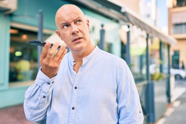 Şehirdeki akıllı telefonu kullanarak ses mesajı gönderen, ciddi ifadeli orta yaşlı kel bir adam..