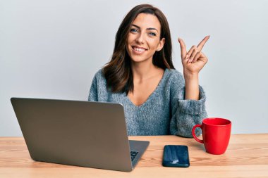 Ofiste çalışan esmer bir kadın bilgisayarını kullanıyor. Gülümsüyor, mutlu bir şekilde elini ve parmağını yan tarafa gösteriyor. 