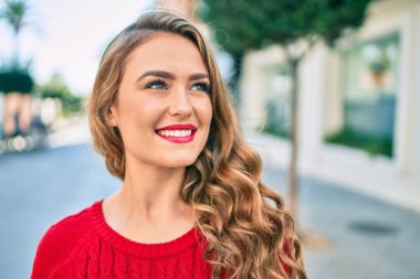 Genç sarışın kız gülümseyerek şehirde mutlu mesut yürüyor..