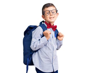 Sevimli sarışın çocuk inek papyonu ve sırt çantası takıyor. Pozitif ve mutlu görünüyor. Kendine güvenen bir gülümsemeyle dişlerini gösteriyor. 