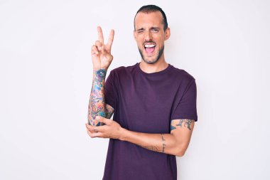 Dövmeli, sıradan kıyafetler giyen, gülümseyen, kameraya göz kırpan ve zafer işareti yapan genç yakışıklı bir adam. İki numara.. 