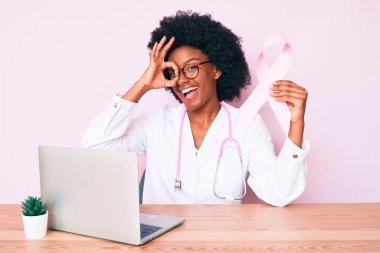 Genç Afro-Amerikan kadın doktor üniforması giyiyor pembe kanser kurdelesi takıyor gülümsüyor. 
