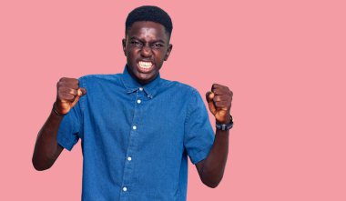 Genç Afro-Amerikalı bir adam günlük kıyafetler giyiyor kızgın ve kızgın yumruklar sallıyor öfkeyle bağırırken sinirli ve öfkeli. öfke ve agresif konsept. 