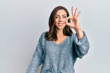 Kışlık süveter giyen genç esmer kadın gülümsüyor ve el ve parmaklarıyla 