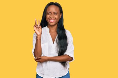 Gündelik kıyafetler giyen, gülen, kameraya göz kırpan, zafer işareti yapan genç siyahi bir kadın. İki numara.. 