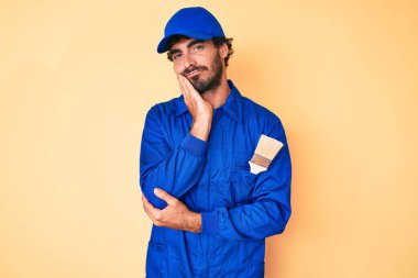 Kıvırcık saçlı ve ayı gibi giyinmiş yakışıklı genç adam çapraz kollu depresyondan sıkılmış ve yorgun göründüğünü düşünüyor.. 