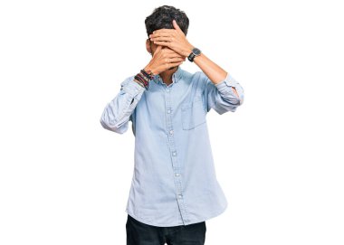 Gündelik kıyafetler giyen genç İspanyol adam gözlerini ve ağzını elleriyle kapatıyor, şaşırmış ve şok olmuş. duygu gizleme 