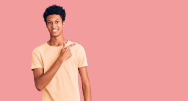 Genç, Afro-Amerikalı, günlük kıyafetler giymiş, neşeli, yüzünde mutlu ve doğal bir ifadeyle, elleri ve parmaklarıyla yüzünü gösteren bir gülümseme olan adam. 