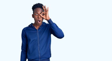 Afro-Amerikalı genç bir adam spor kıyafetleri giyiyor. Şaşırmış yüz ifadesiyle şaşırmış, parmaklarının arasından bakıyor. İnançsız ifade. 