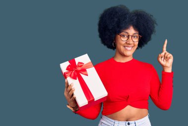 Genç Afro-Amerikalı kız elinde hediye tutarak başarılı bir fikir gösterdi. Heyecanlı ve mutlu. Bir numara.. 