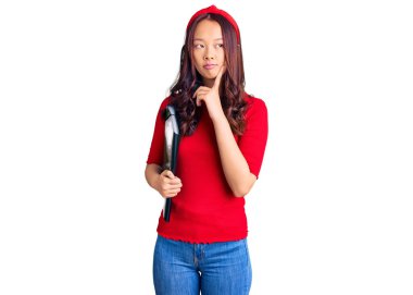 Öğrenci klasörü takan genç, güzel Çinli bir kız. Ciddi bir yüz ifadesi. Elleri çenesinde soru sormayı düşünüyor. 