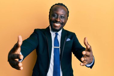 Yakışıklı, takım elbiseli ve kravatlı genç bir adam kameraya bakıp kucaklaşmak için gülümsüyor. Mutluluğu kucaklayan neşeli bir ifade.. 