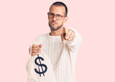 Elinde dolar sembolü olan genç ve yakışıklı bir adam kamerayı işaret ediyor. Kendine güvenen bir jest, ciddi görünüyor. 