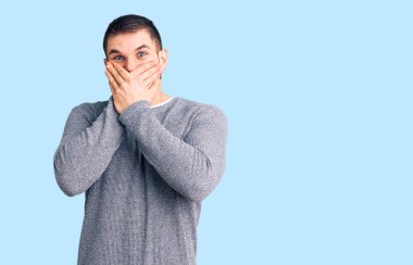 Gündelik kazak giyen genç yakışıklı adam yanlışlıkla elleri ile ağzını kapatırken şok oldu. gizli kavram. 