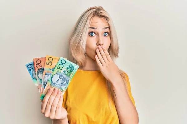 Piękna Biała Blondynka Trzymająca Australijskie Dolary Zakrywające Usta Ręką Zszokowana — Zdjęcie stockowe