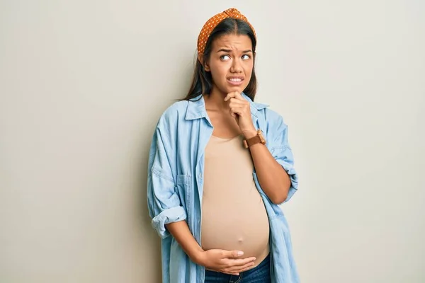 赤ちゃんを期待している美しいヒスパニック系の女性 質問を心配し 妊娠中の腹に触れます 顎に手で心配し — ストック写真