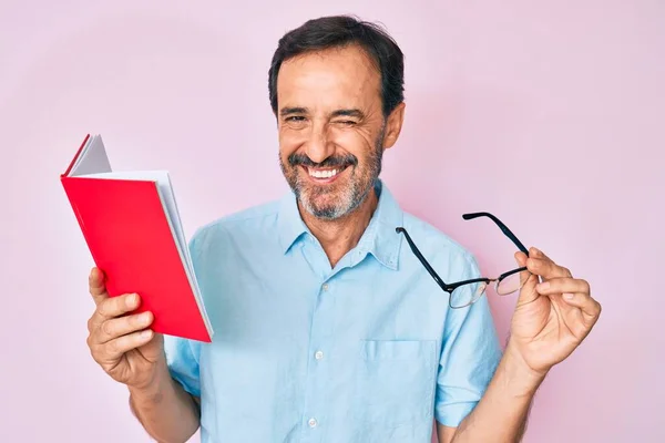 Hombre Hispano Mediana Edad Leyendo Libro Sosteniendo Gafas Guiñando Ojo — Foto de Stock