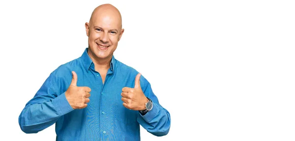 Middle age bald man wearing casual clothes success sign doing positive gesture with hand, thumbs up smiling and happy. cheerful expression and winner gesture.