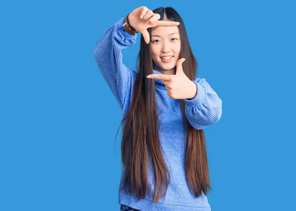 Young beautiful chinese woman wearing casual turtleneck sweater smiling making frame with hands and fingers with happy face. creativity and photography concept.