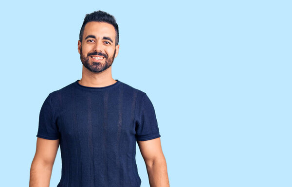 Молодой латиноамериканец в повседневной одежде выглядит позитивно и счастливо стоя и улыбаясь с уверенной улыбкой, показывая зубы 