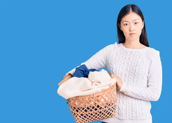 若い美しい中国の女性は服を着て洗濯バスケットを保持考え態度と落ち着いた表情は自信を持って見て — ストック写真
