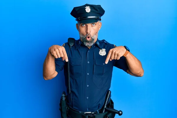 Middle age handsome man wearing police uniform pointing down with fingers showing advertisement, surprised face and open mouth