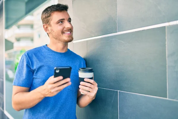 若い白人男性がスマートフォンを使って街でコーヒーを飲んでいます — ストック写真
