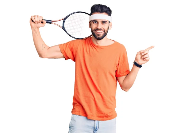 年轻英俊的男人 留着胡子打网球 手里拿着球拍 面带微笑 手指手画脚地指向旁边 — 图库照片