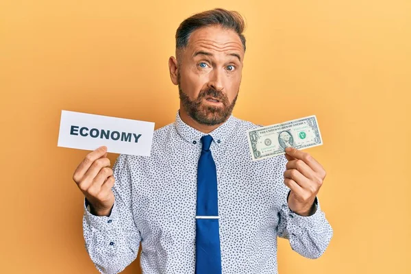 ハンサムな中年の男性が経済メッセージを保持し 1ドルの無知で混乱した表現を保持する 疑わしい概念 — ストック写真