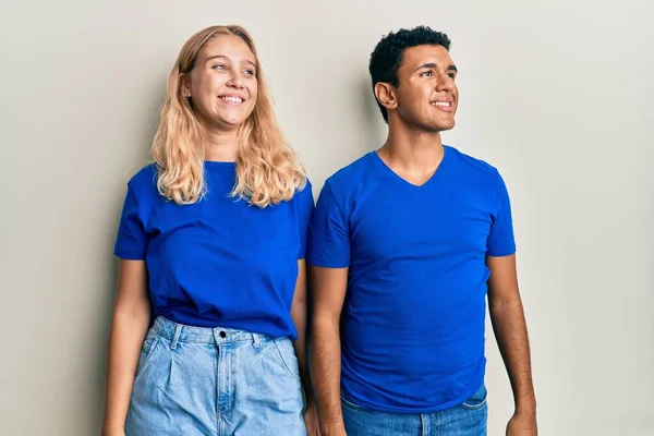 Young interracial couple wearing casual clothes looking away to side with smile on face, natural expression. laughing confident.
