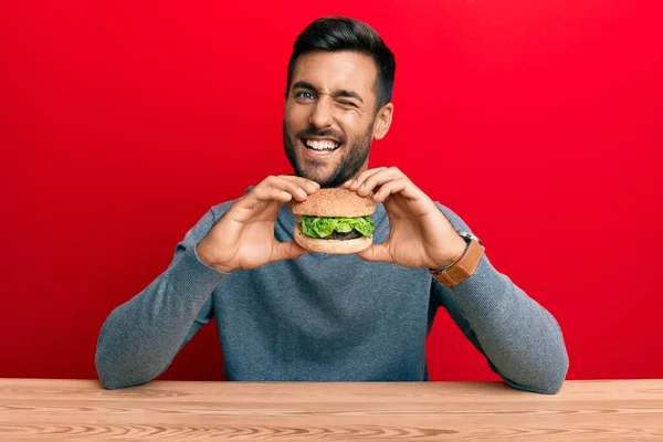 Hombre Hispano Guapo Comiendo Una Sabrosa Hamburguesa Clásica Guiñando Ojo — Foto de Stock