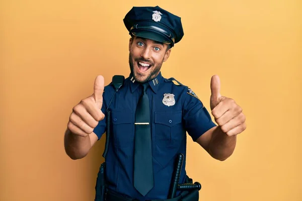 Handsome hispanic man wearing police uniform approving doing positive gesture with hand, thumbs up smiling and happy for success. winner gesture.