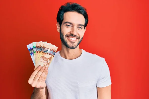 Ung Latinamerikansk Man Håller Kanadensiska Dollar Ser Positiv Och Glad — Stockfoto