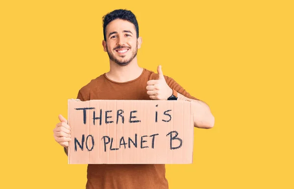 Young hispanic man holding there is no planet b banner smiling happy and positive, thumb up doing excellent and approval sign