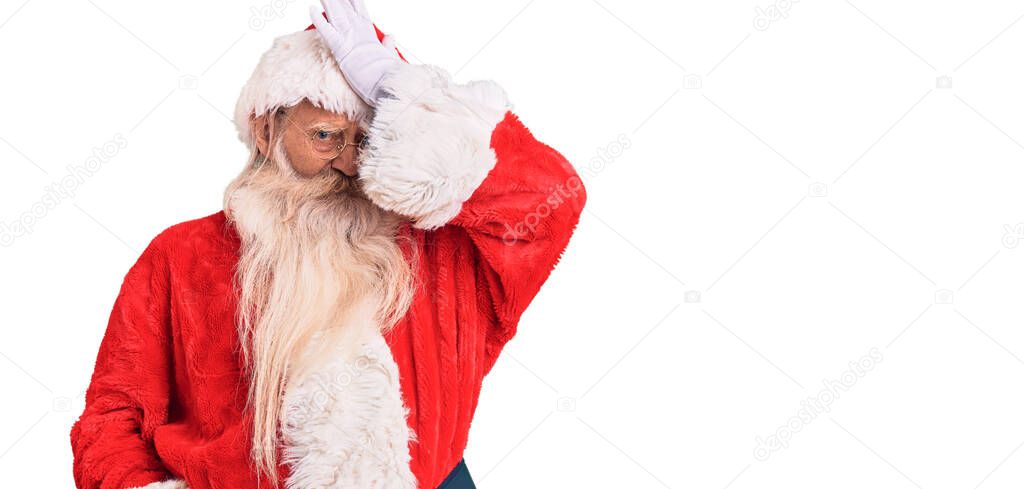 Old senior man with grey hair and long beard wearing traditional santa claus costume surprised with hand on head for mistake, remember error. forgot, bad memory concept. 