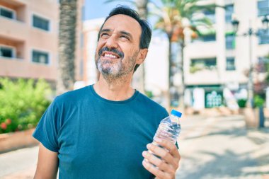 Orta yaşlı, sakallı, mutlu, açık havada su içen bir adam.