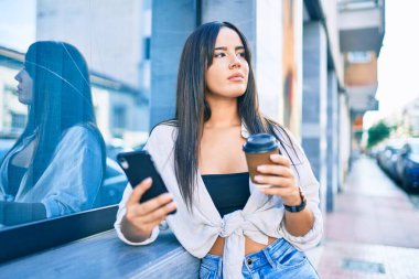 Genç İspanyol kız şehirde akıllı telefon kullanarak mutlu bir şekilde gülümsüyor..