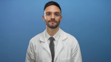 İspanyol erkek doktor gözlük takıyor ve mavi arka planda steteskop takan beyaz önlüklü, profesyonellik ve tıbbi uzmanlık taşıyor..