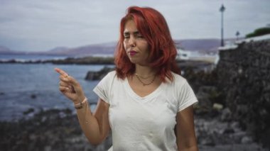 Genç İspanyol kadın sahil kenarındaki duvar ve lamba direğini işaret ediyor; tamamen onaylanmamış..