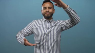 Adam görünmez bir objeyi elleriyle çerçeveletiyor ve bir stüdyoda mavi bir arkaplan karşısında gülümsüyor; güven sunumu.