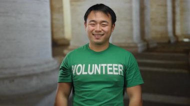 Gönüllü gömleği giyen genç adam kilisenin içinde kendine güvenen bir görünüm sergiliyor, toplum içinde yer alıyor ve kapalı bir alanda hayır işi yapıyor..