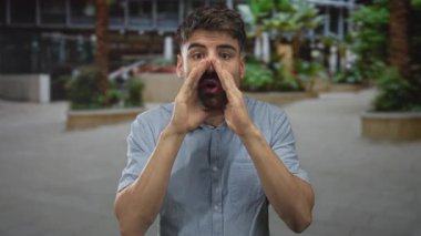 Adam kentin işlek caddesinde palmiye ağaçlarıyla kaplı açık mavi bir gömlek giyerek kendini işaret ediyor..