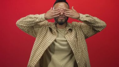 Ekose gömlekli, elleri suratında ve avuçlarını kaldırmış kırmızı stüdyoda ağzı açık, sürpriz mucize enerjili bir adam..