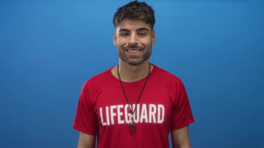 Genç İspanyol cankurtaranın eli, mavi stüdyo duvarına karşı kırmızı tişörtün üzerinde ıslıkla imza atıyor..