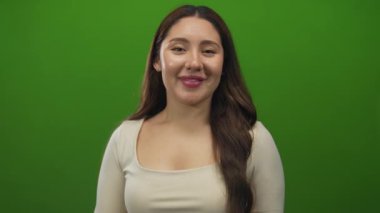 Uzun siyah saçlı İspanyol kadın gülümser ve parlak yeşil stüdyoda başparmak kaldırır; iyimserlik.