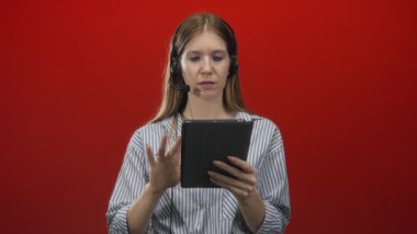 Sarı saçlı, kulaklık takan, kırmızı stüdyoda dijital tablete işaret eden bir kadın. Konsantrasyon öğreniyor..