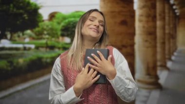 Bir kadın gülümsüyor ve bir kitabı kucaklıyor şehir sokaklarında dikilirken, şehir ortamında neşeli hissederken..